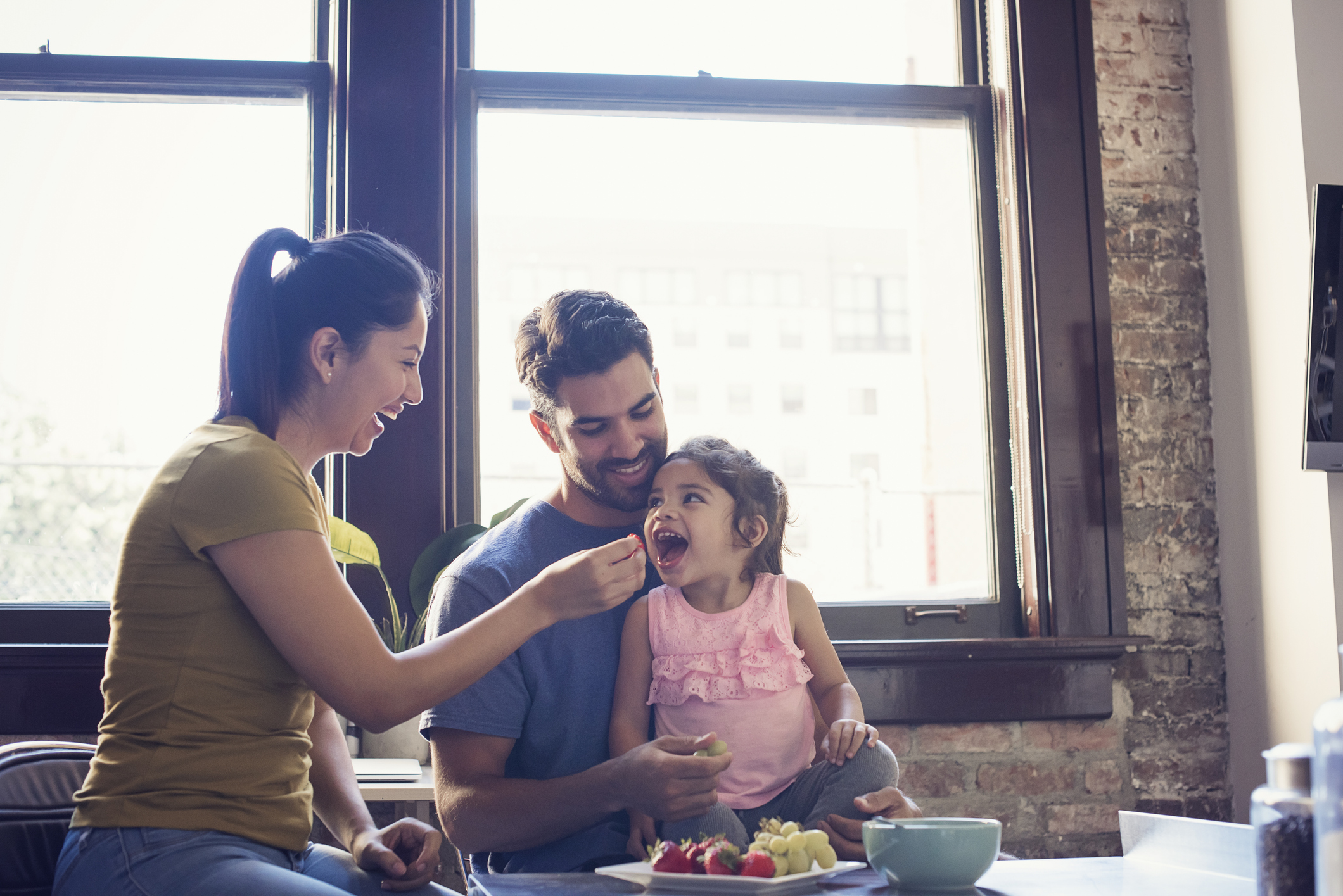 Mother and father feeding their little daughter in kitchen