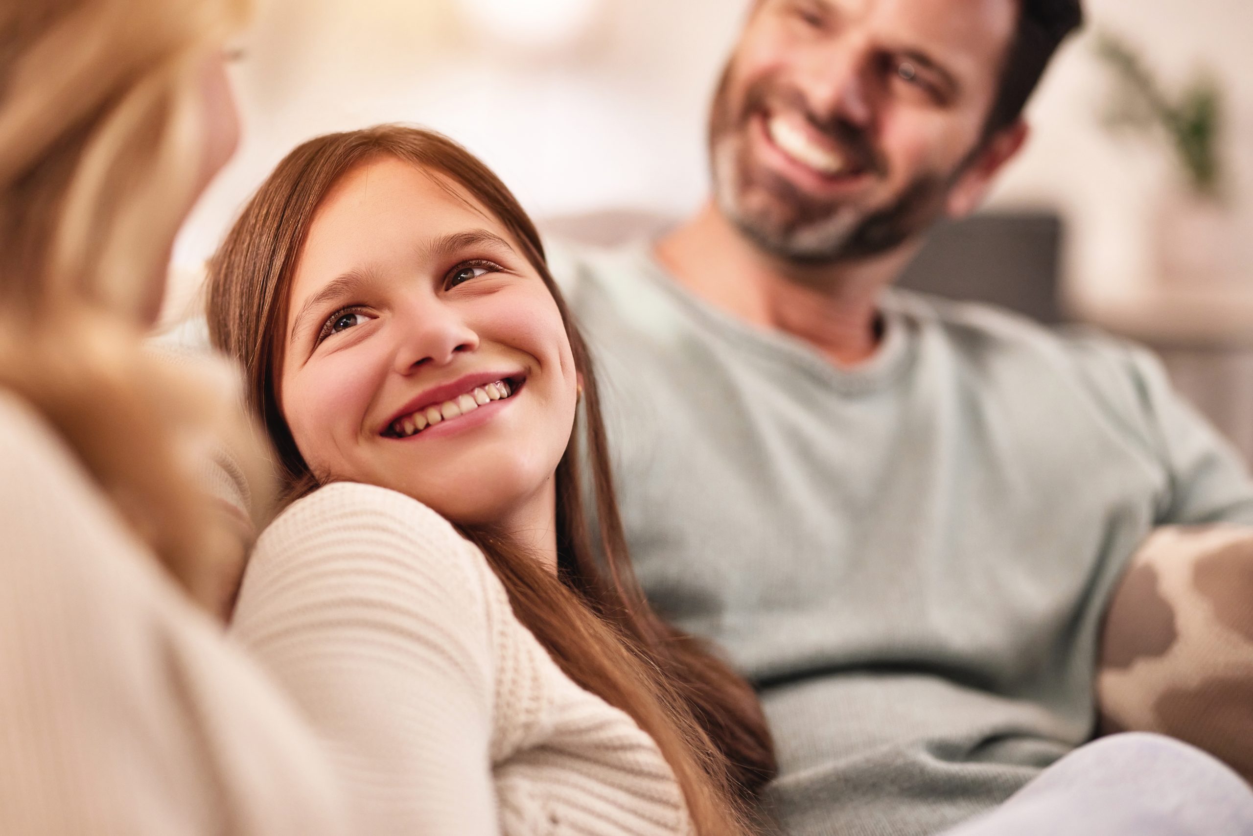 Happy man, woman and teenager girl on sofa with smile, conversation and quality time to relax at night in family home. Father, mother and daughter on couch, laughing together and bonding in happiness